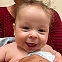 Milo is registered to the contest to win money with this photo: baby, smiling, curly_hair, person, holding, hand, tattoo, blanket, red_shirt, striped_shirt, close_up, face, happy, infant, skin, indoor, child, portrait, cute, expression