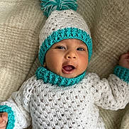 Ansh joined the competition — help win amazing prizes! baby, child, crochet, hat, pom_pom, white, teal, sweater, smiling, mouth_open, lying_down, blanket, warm, cozy, cute, infant, face, headwear, knitted, soft