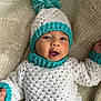 baby, child, crochet, hat, pom_pom, white, teal, sweater, smiling, mouth_open, lying_down, blanket, warm, cozy, cute, infant, face, headwear, knitted, soft
