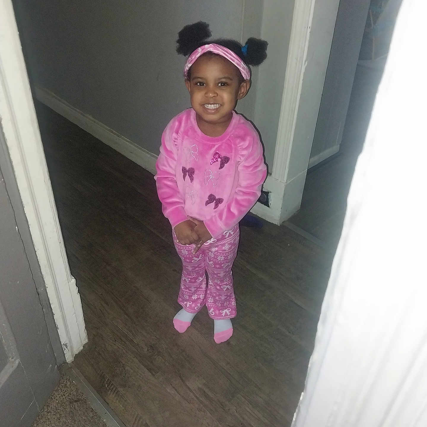Teneyah joined the competition — help win amazing prizes! child, girl, smile, pajamas, pink_clothing, headband, pigtails, indoors, hallway, wood_floor, carpet, doorframe, standing, happy, person, young_child, cute, portrait, home, fashion