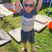 Johnathan is registered to the contest to win money with this photo: child, boy, sunglasses, outdoor, grass, shadow, sunlight, tshirt, shorts, barefoot, toy, cushion, swing, playground, backyard, summer, person, standing, happy, casual