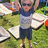 child, boy, sunglasses, outdoor, grass, shadow, sunlight, tshirt, shorts, barefoot, toy, cushion, swing, playground, backyard, summer, person, standing, happy, casual