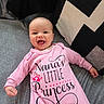 baby, infant, smiling, onesie, pink_clothing, couch, pillow, geometric_pattern, happy, portrait, indoor, child, cute, face, person, lying_down, cozy, soft_fabric, home, newborn