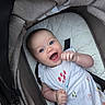 baby, child, smiling, happy, stroller, cushion, blue_eyes, white_dress, patterned_clothing, infant, cute, portrait, person, seated, hand, face, head, outdoor, fabric, comfort