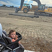 Luciano joined the competition — help win amazing prizes! toddler, child, stroller, sidewalk, construction_site, excavator, dirt, pipes, cloudy_sky, outdoor, person, young_child, machine, earth, vehicle, equipment, daylight, casual_clothing, curious, urban