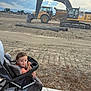 toddler, child, stroller, sidewalk, construction_site, excavator, dirt, pipes, cloudy_sky, outdoor, person, young_child, machine, earth, vehicle, equipment, daylight, casual_clothing, curious, urban