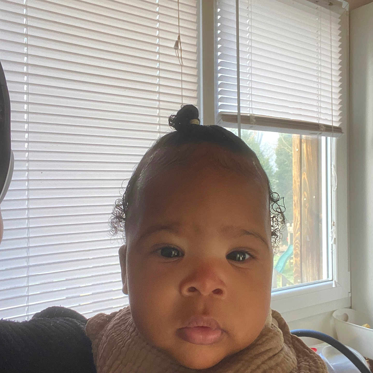 Jahëlya a rejoint le concours — aidez-le/la à gagner de superbes lots ! baby, child, face, portrait, indoors, window, blinds, natural_light, curly_hair, top_knot, bib, clothing, person, young_child, close_up, expression, skin, head, eye, cute