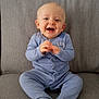 baby, child, smiling, blue_onesie, sitting, clapping_hands, happy, face, cute, infant, couch, furniture, indoors, cozy, young_child, portrait, expression, skin, head, eyes