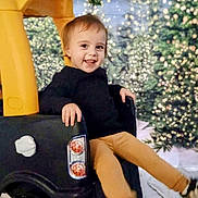Aubrey is registered to the contest to win money with this photo: child, toddler, toy_car, smile, christmas_tree, holiday_lights, bokeh, festive, winter_scene, play, indoor, sweater, pants, sneakers, seat, happy, portrait, background, decoration, candid