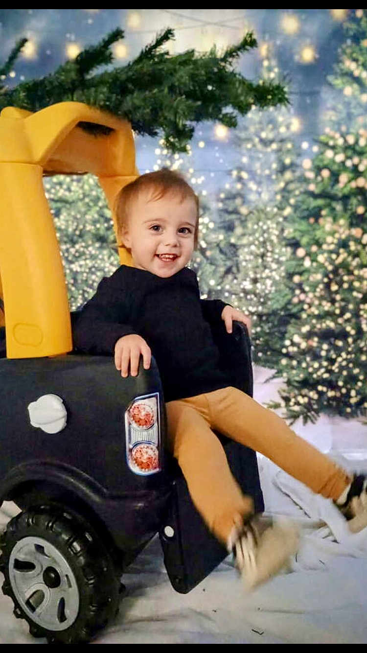 Aubrey is registered to the contest to win money with this photo: child, toddler, toy_car, smile, christmas_tree, holiday_lights, bokeh, festive, winter_scene, play, indoor, sweater, pants, sneakers, seat, happy, portrait, background, decoration, candid