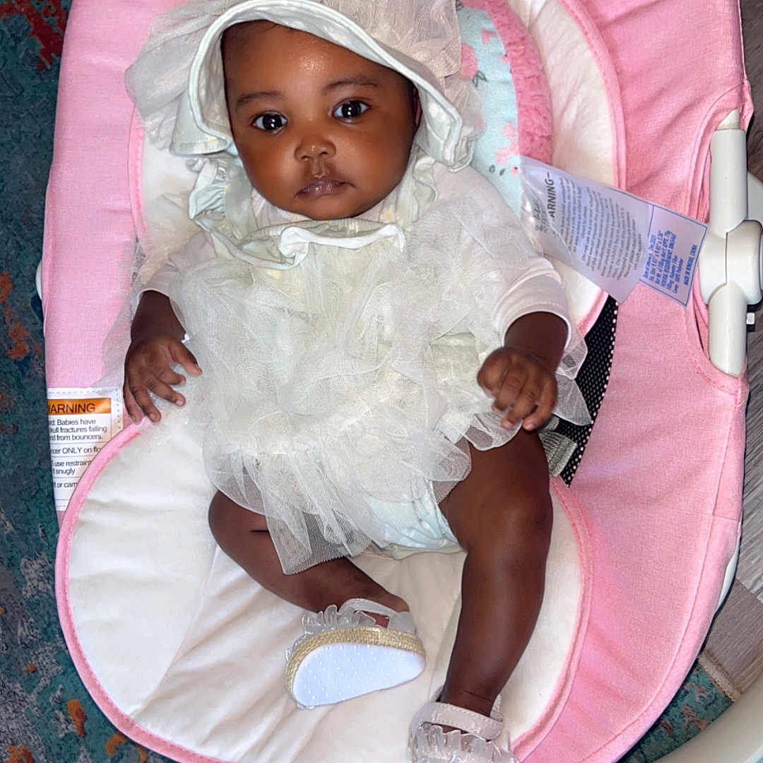 Jersi joined the competition — help win amazing prizes! adorable, baby, baby_shoes, bonnet, carpet, child, cute, flooring, footwear, home, indoors, infant, looking_at_camera, person, pink_baby_seat, portrait, resting, seated, soft_fabric, white_dress