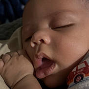 Caspian joined the competition — help win amazing prizes! baby, infant, sleeping, yawning, portrait, face, closed_eyes, hand, fist, blanket, clothing, indoors, close_up, cozy, dim_lighting, peaceful, resting, short_sleeves, red_shirt, photography
