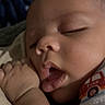 baby, infant, sleeping, yawning, portrait, face, closed_eyes, hand, fist, blanket, clothing, indoors, close_up, cozy, dim_lighting, peaceful, resting, short_sleeves, red_shirt, photography