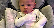 Caspian is registered to the contest to win money with this photo: baby, infant, child, car_seat, portrait, face, wide_eyes, serious_expression, seated, harness, cushion, headrest, padded_seat, long_sleeves, white_clothing, indoor, close_up, front_facing, colorful_lighting, photography