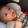baby, infant, child, car_seat, seatbelt, buckled, portrait, close_up, indoors, vehicle, red_shirt, gray_harness, cushion, sitting, looking_at_camera, face, eyes, hand, safety_label, photography