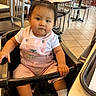 baby, bow, casual_dining, chair, child, curious_expression, cute, floor_tiles, food_court, high_chair, indoor, people, person, pink_overalls, pony_tail, restaurant, sitting, table, toddler, white_shirt