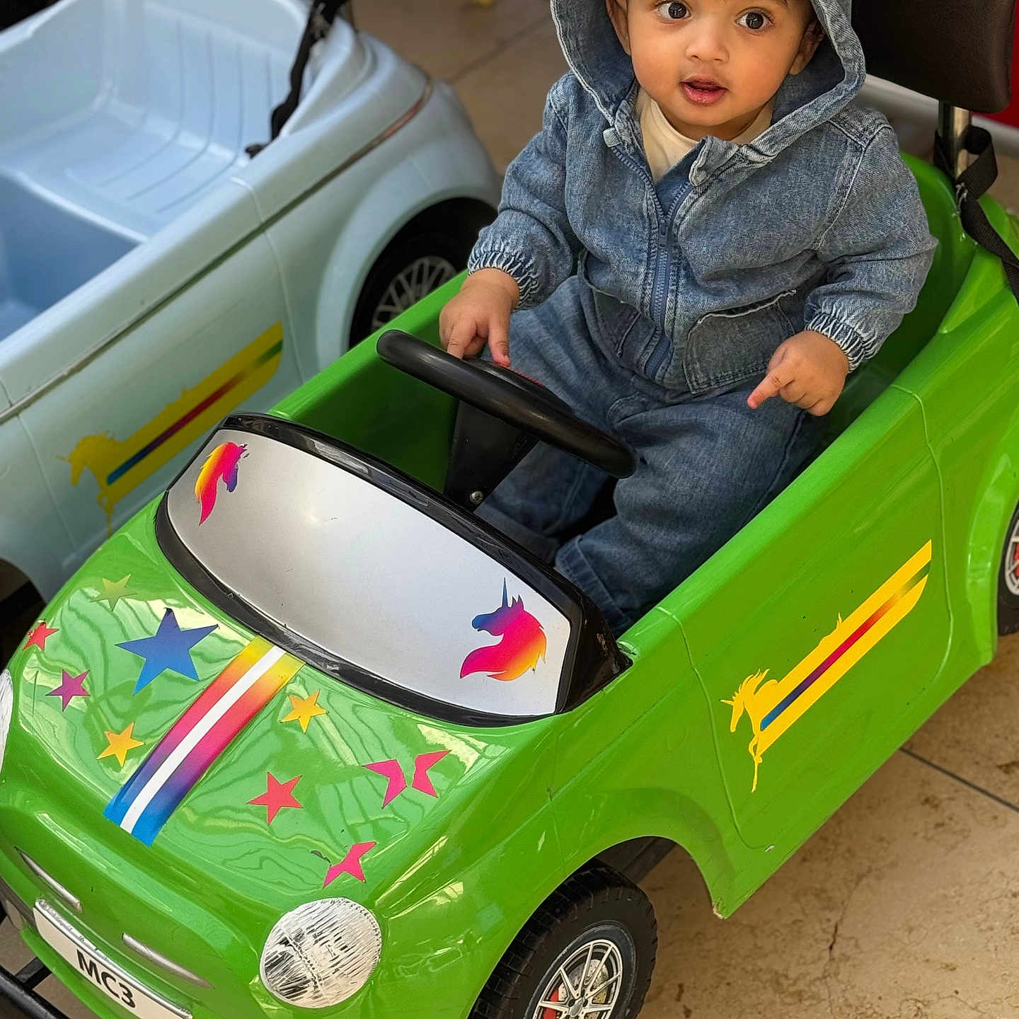 Saad joined the competition — help win amazing prizes! toddler, child, denim_hoodie, toy_car, green_car, unicorn_stickers, stars, indoor, floor_tiles, small_wheels, steering_wheel, cute_expression, casual_clothing, playtime, vehicle_toy, kid_playing, seat, hood, bright_colors, imaginative_play