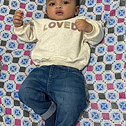 Saad is registered to the contest to win money with this photo: baby, child, infant, sweater, denim_jeans, blanket, patterned, lying_down, curious, indoors, portrait, casual_clothing, cute, young_child, face, hands, feet, relaxed, comfortable, closeup