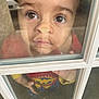 child, toddler, face, window, glass, reflection, curious, wonder_woman, costume, red_clothing, yellow_clothing, blue_clothing, indoor, hand, expression, closeup, portrait, person, young_child, casual