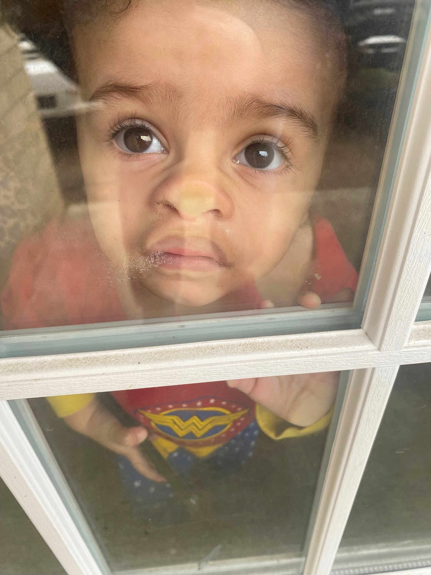 Wrenley joined the competition — help win amazing prizes! child, toddler, face, window, glass, reflection, curious, wonder_woman, costume, red_clothing, yellow_clothing, blue_clothing, indoor, hand, expression, closeup, portrait, person, young_child, casual