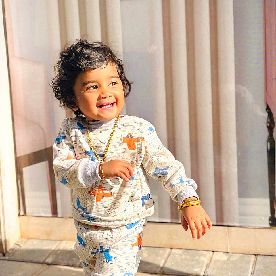 Kiara Elen is registered to the contest to win money with this photo: airplane, bracelet, child, clothing, curly_hair, curtain, cute, daylight, gold_jewelry, happy, necklace, outdoor, pattern, pavement, person, smiling, sunlight, toddler, tracksuit, walking