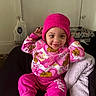 Diana is registered to the contest to win money with this photo: blanket, child, cozy, cute, face, furniture, happy, hat, home, indoors, long_sleeve_shirt, pants, person, pink_clothing, playful, sitting, smiling, toddler, warm_clothing, young_child