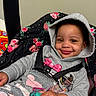 baby, blanket, car_seat, child, clothing, cozy, cute, face, floral_pattern, happy, hoodie, indoor, infant, pacifier, person, portrait, seatbelt, smile, toddler, toy