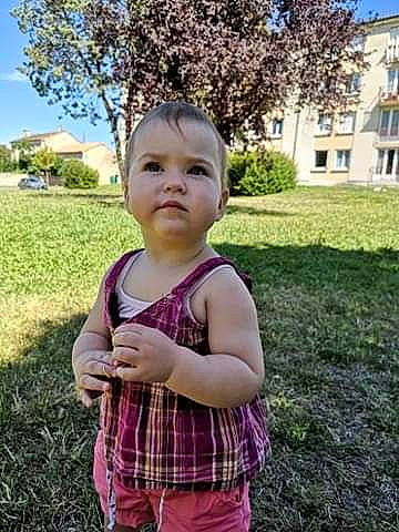 Athéna a rejoint le concours — aidez-le/la à gagner de superbes lots ! baby, baby_toddler_clothing, child, facial_expression, gesture, grass, happy, leisure, people_in_nature, person, pink, plaid, plant, recreation, sky, standing, summer, tartan, toddler, tree