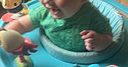 Slade joined the competition — help win amazing prizes! activity_center, baby, child, colorful, cushion, face, furniture, green_shirt, happy, head, indoor, infant, laughing, living_room, person, plastic_toys, play, seat, smile, toy
