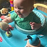 Slade joined the competition — help win amazing prizes! baby, child, toy, activity_center, green_shirt, laughing, indoor, play, happy, person, furniture, living_room, colorful, plastic_toys, seat, cushion, head, face, smile, infant