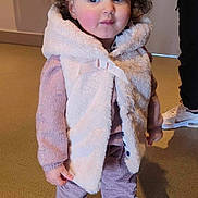 Lina a rejoint le concours — aidez-le/la à gagner de superbes lots ! toddler, child, curly_hair, indoor, vest, pink_sweater, pants, white_shoes, person, standing, floor, curious_expression, clothing, portrait, young_child, headband, fashion, casual, cute, shoes