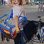 Lina participe au concours pour gagner de l'argent avec cette photo : child, toddler, pony, animal, hat, curly_hair, night, outdoor, people, trees, street, pavement, festive, riding, saddle, colorful, footwear, holding, reins, park