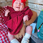 Lou a rejoint le concours — aidez-le/la à gagner de superbes lots ! baby, child, red_clothing, headband, bow, white_shoes, socks, smiling, closed_eyes, holding, hand, tattoo, checkered_shirt, wooden_wall, indoor, person, happy, cute, portrait, infant