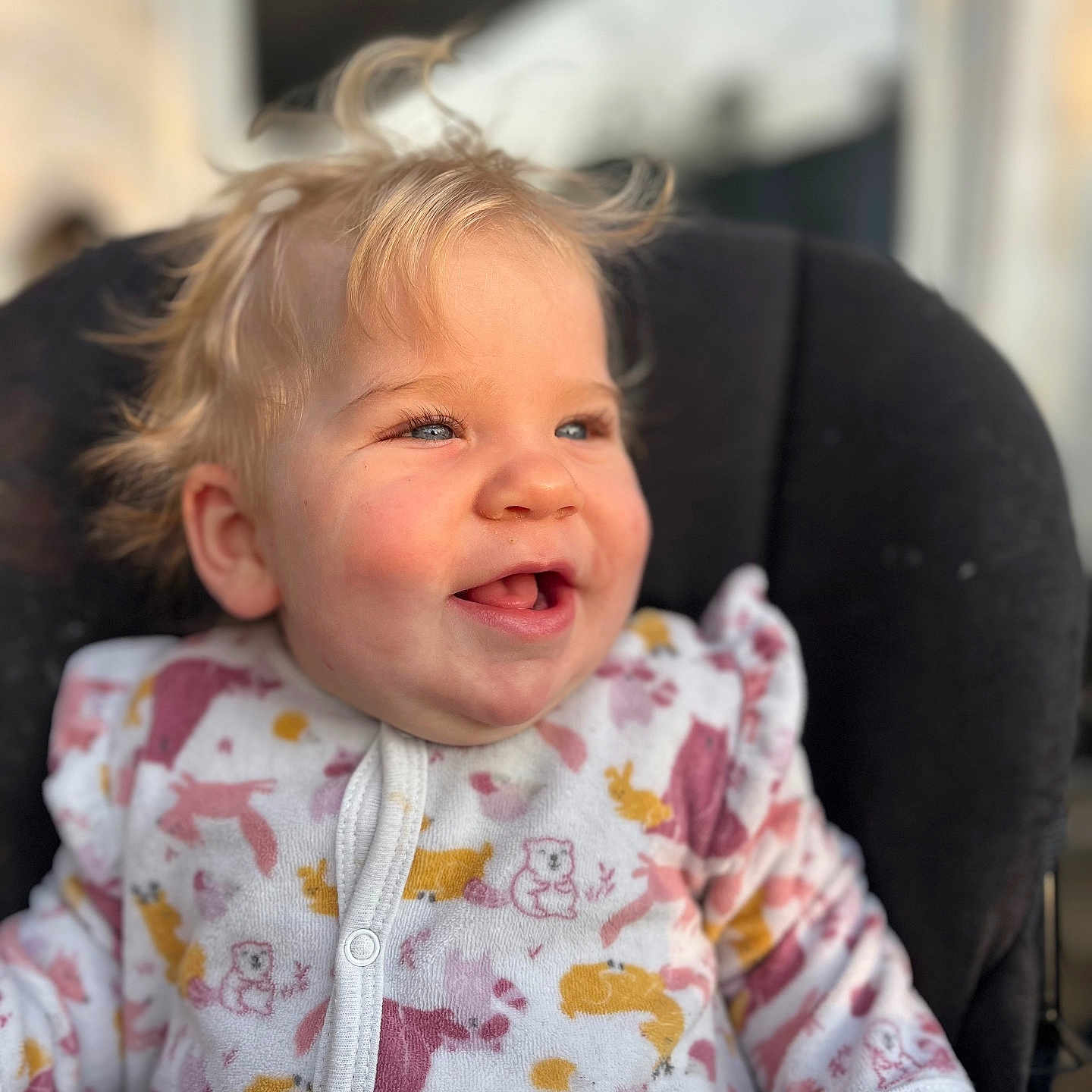 Lyana participe au concours pour gagner de l'argent avec cette photo : animal_print, baby, blonde_hair, blue_eyes, chair, child, close_up, clothing, cushion, cute, face, happy, indoor, infant, onesie, portrait, sitting, smiling, soft_light, toddler