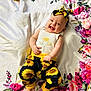 baby, child, smiling, flower_pattern, headband, sunflower, pants, white_shirt, blanket, floral, happy, cute, infant, playful, indoors, colorful, person, portrait, lying_down, cheerful