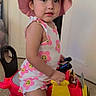 toddler, child, pink_hat, floral_romper, toy_airplane, indoor, carpet, mickey_mouse, wheels, yellow, red, smiling, cute, play, hat, face, person, young_child, home, fun