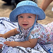 Leya a rejoint le concours — aidez-le/la à gagner de superbes lots ! baby, child, blue_hat, floral_shirt, blanket, outdoor, beach, sunhat, face, smiling, lying_down, patterned_blanket, skin, arm, person, photography, young_child, closeup, summer, daylight