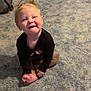 toddler, child, smiling, sitting, carpet, indoor, baby_gate, storage_drawer, black_shirt, blond_hair, pigtails, happy, person, floor, room, casual_clothing, footwear, playful, cute, young_child