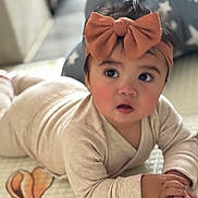 Vivienne is registered to the contest to win money with this photo: baby, child, headband, bow, tummy, lying_down, indoors, soft_lighting, cushion, star_pattern, cozy, curious, wide_eyes, clothing, infant, person, portrait, cute, skin, hands