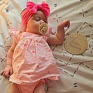 Luna Ray is registered to the contest to win money with this photo: baby, baby_fashion, blanket, child, dress, face, family_photo, headband, indoor, infant, lying_down, milestone_photo, onesie, pacifier, patterned_background, pink_bow, portrait, six_months, sleeping, wooden_sign