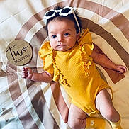 Sakari is registered to the contest to win money with this photo: baby, infant, yellow_clothing, socks, sunglasses, sign, milestone, two_months, round_mat, rainbow_pattern, star_pattern, lying_down, cute, child, person, indoors, soft_lighting, portrait, young, celebration