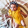 baby, infant, yellow_clothing, socks, sunglasses, sign, milestone, two_months, round_mat, rainbow_pattern, star_pattern, lying_down, cute, child, person, indoors, soft_lighting, portrait, young, celebration