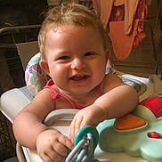 Nevaeh-Rae joined the competition — help win amazing prizes! baby, child, high_chair, toy, smile, happy, indoor, curly_hair, blonde, play, person, clothing, furniture, household, hand, face, cute, infant, cheerful, domestic