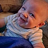 Caleb is registered to the contest to win money with this photo: baby, smiling, blanket, striped_shirt, pillow, indoor, child, happy, cute, infant, person, portrait, cozy, young_child, skin, head, arm, seated, relaxed, home
