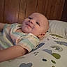 baby, child, infant, smile, pillow, pattern, wood_paneling, bedroom, soft_lighting, lying_down, clothing, short_sleeves, face, head, skin, person, cute, happy, indoors, comfort