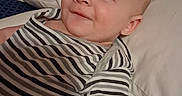 Caleb is registered to the contest to win money with this photo: baby, infant, striped_clothing, smile, face, head, eyes, bed, pillow, sleepwear, skin, cute, child, person, lying_down, indoors, young, happy, portrait, apparel