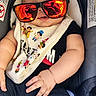 accessory, baby, bib, car_seat, casual, child, clothing, cute, fashion, footwear, hand, indoors, infant, legs, person, reflection, relaxed, seat, smiling, sunglasses