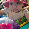 baby, child, red_hat, toy, indoor, face, curious, playtime, colorful, table, plastic_toy, infant, person, clothing, dome, smile, background, household, furniture, closeup