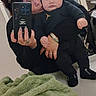 accessories, baby, bathroom, black_clothing, blanket, casual, countertop, expressionless, face, hand, hoodie, indoor, mirror, mirror_reflection, person, selfie, smartphone, sunglasses, toddler, woman