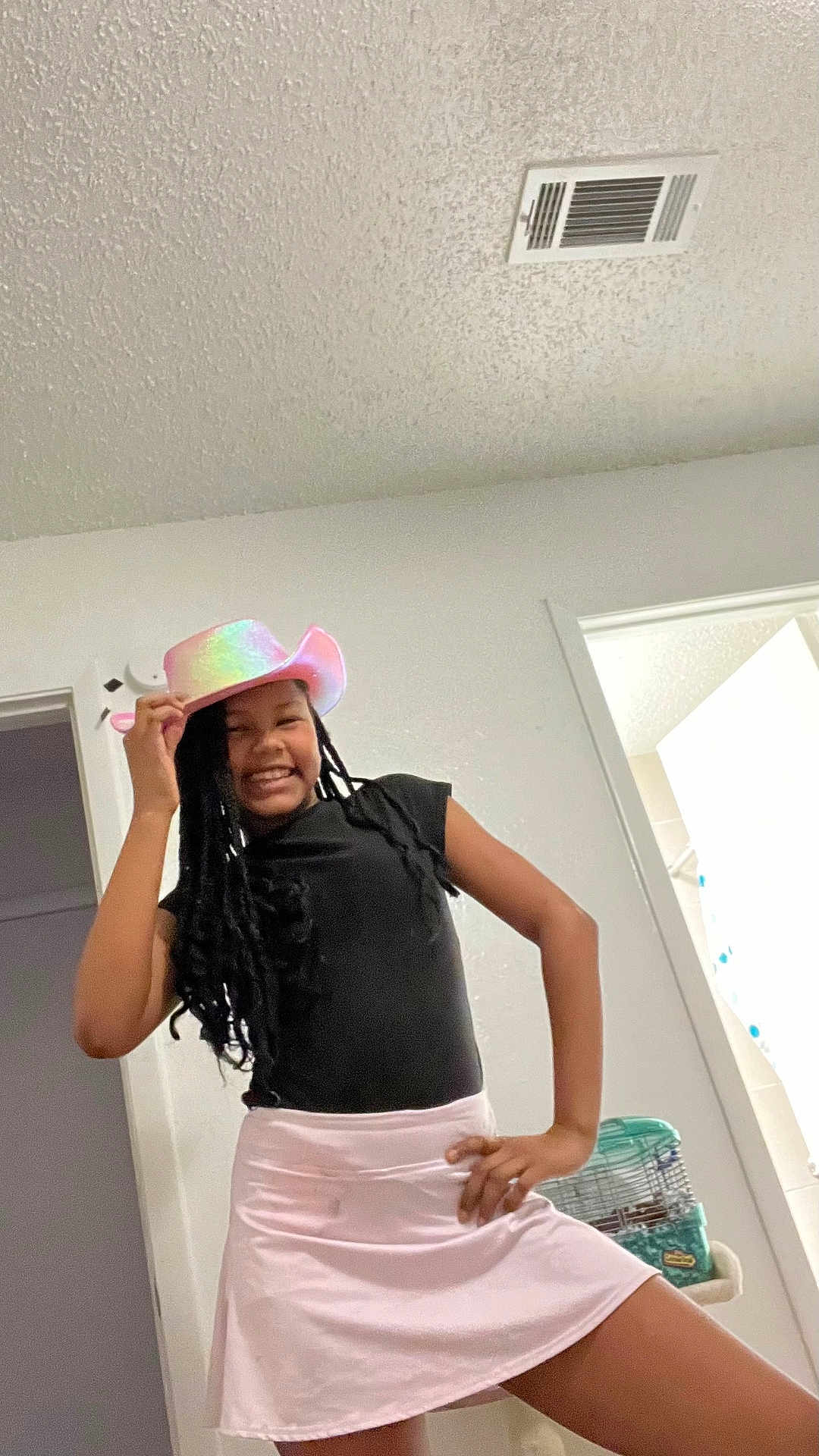 Brooklyn is registered to the contest to win money with this photo: child, girl, smile, braids, hat, cowboy_hat, pastel_hat, black_shirt, pink_skirt, indoor, ceiling, vent, doorway, pet_cage, hamster_cage, pose, playful, grin, standing, home_interior